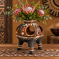 Front view of tribal globe cut-out wooden vase with king proteas and wattle on a tribal rug in warm ambient light