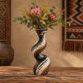 Full view of African tribal eye twist wooden vase with proteas and yellow wattle on a tribal rug beside African wall decor